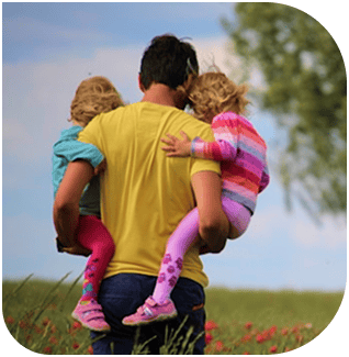 Child and adult holding two kids dressed as dinosaurs outdoors.