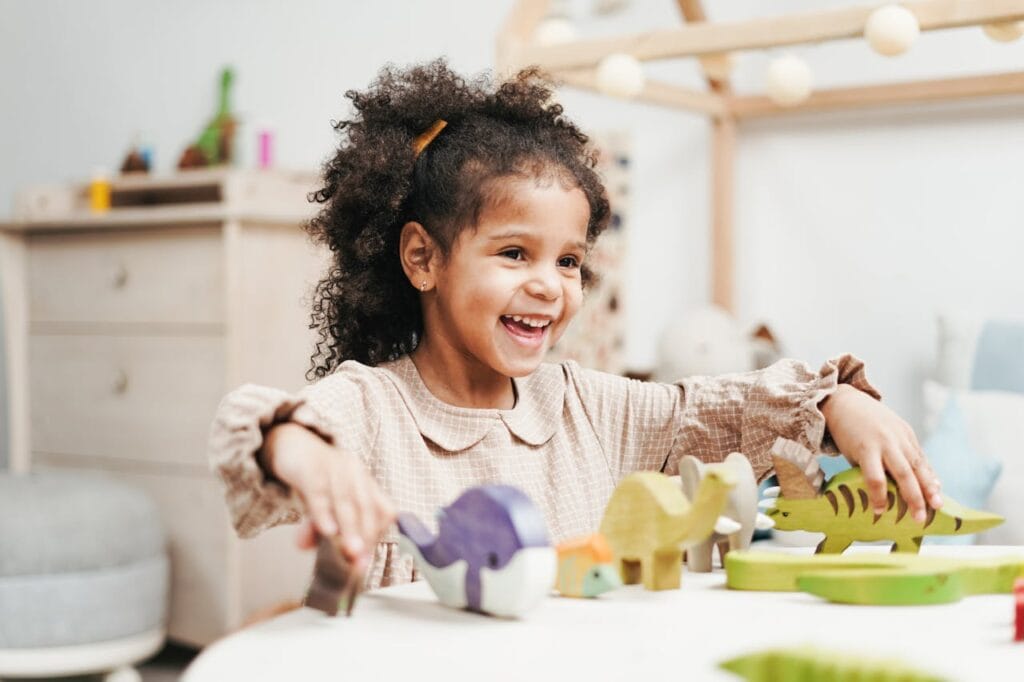Young girl playing with colorful dinosaur toys in a bright, welcoming classroom.